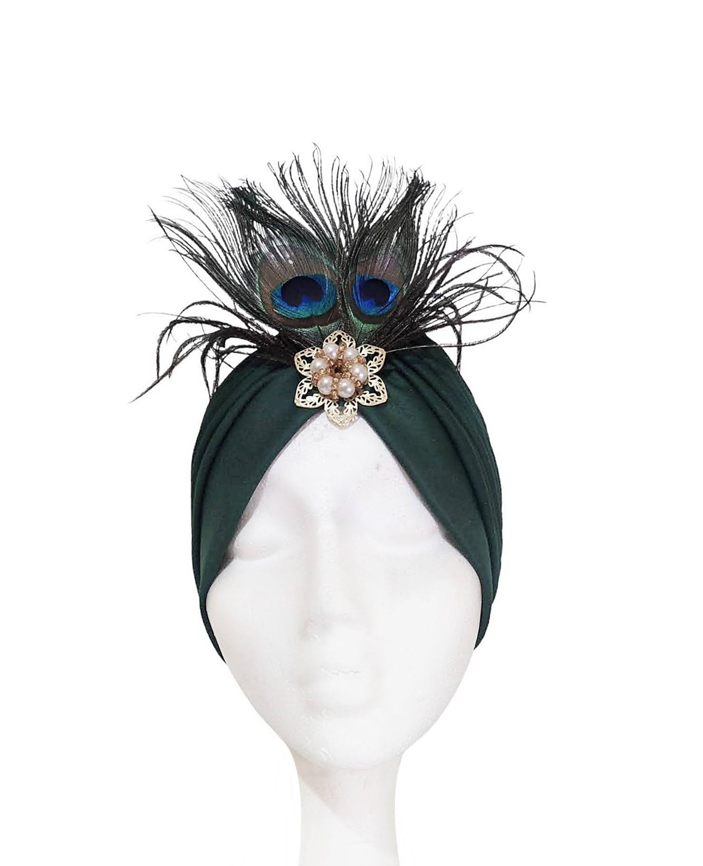 Vista frontal del turbante verde oscuro con plumas y broche centrado en la cabeza del maniquí.