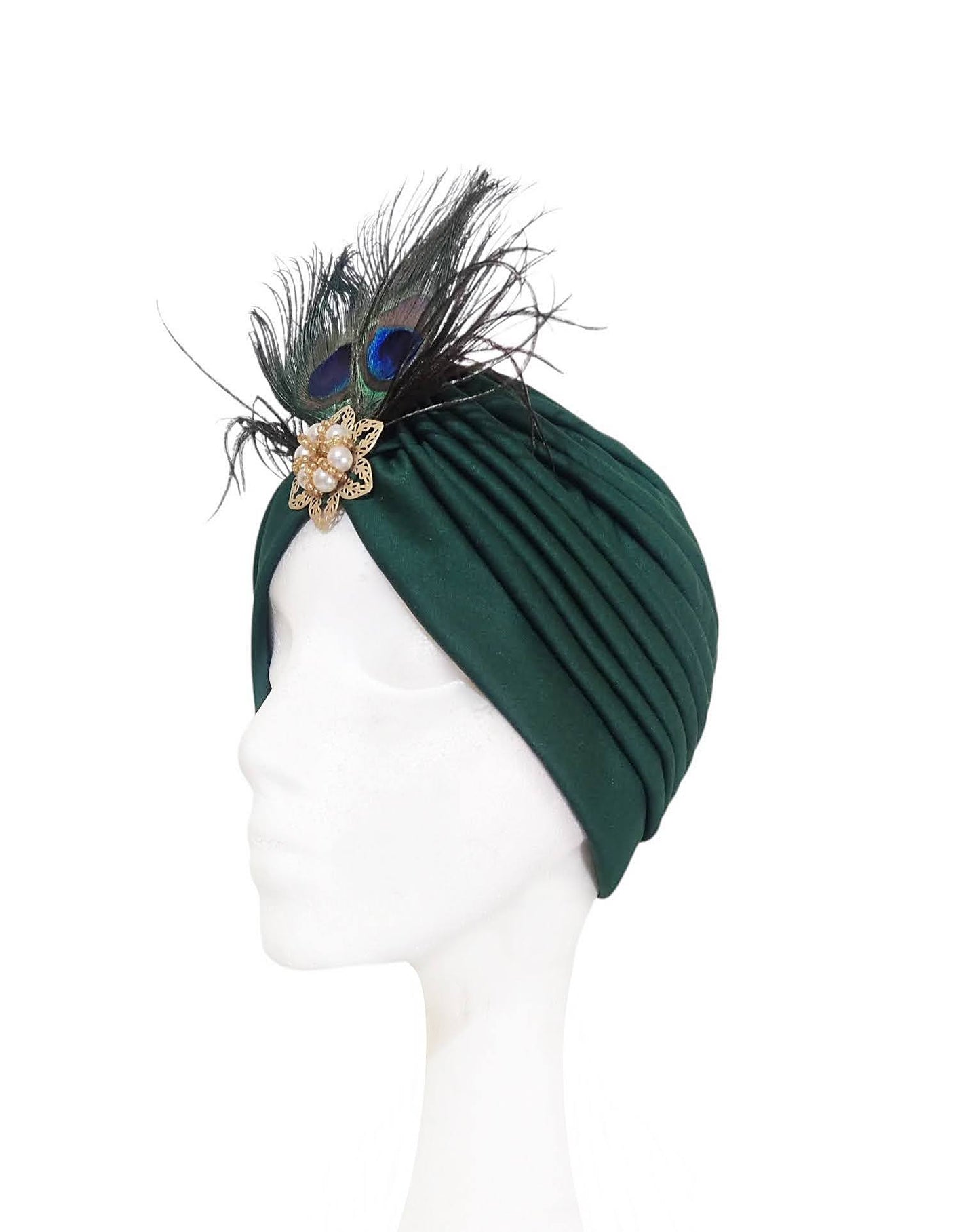 Vista lateral derecha del turbante verde oscuro con plumas y broche dorado.