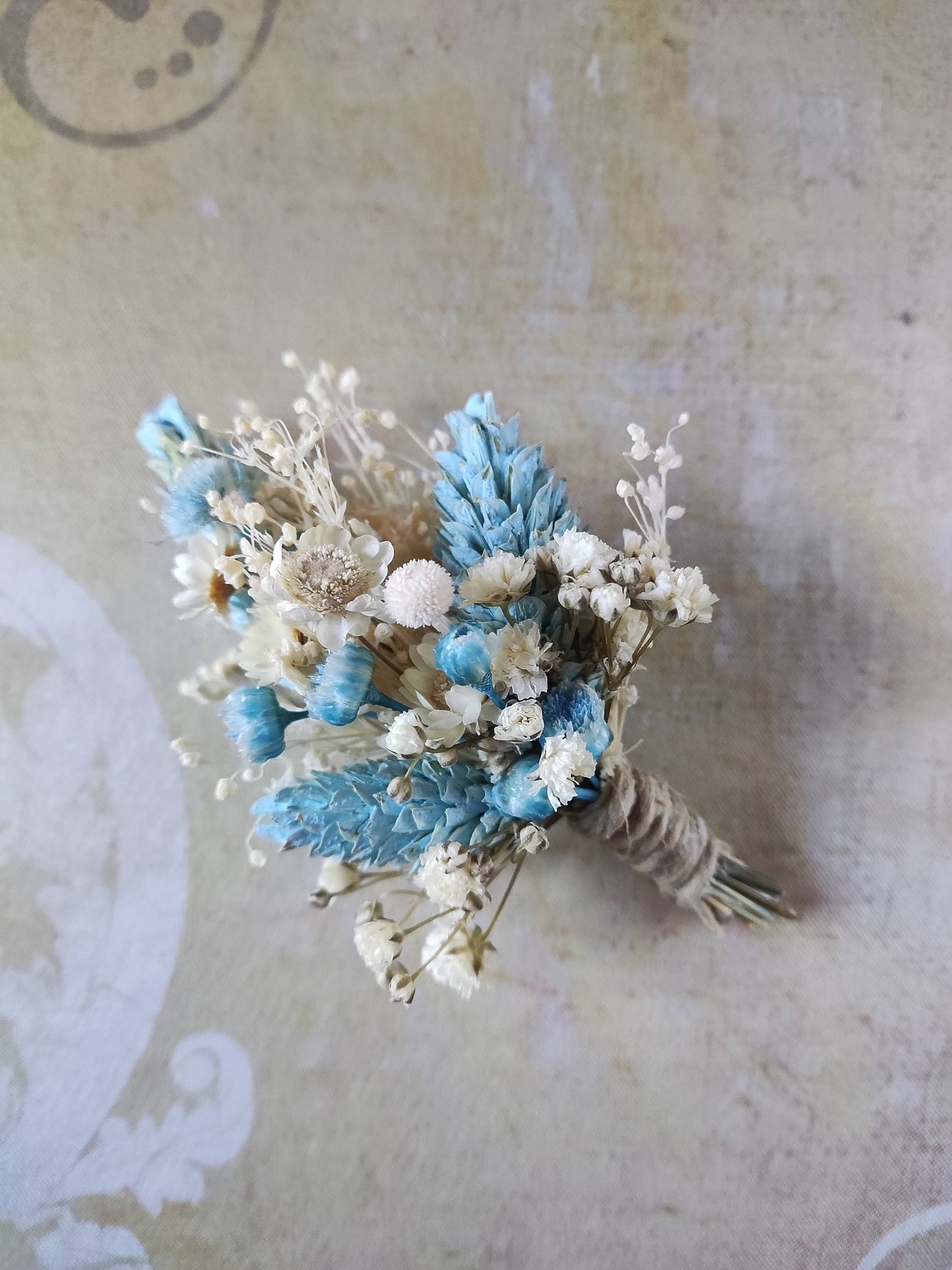 Primer plano del boutonniere en tonos azul celeste y marfil sobre fondo neutro.
