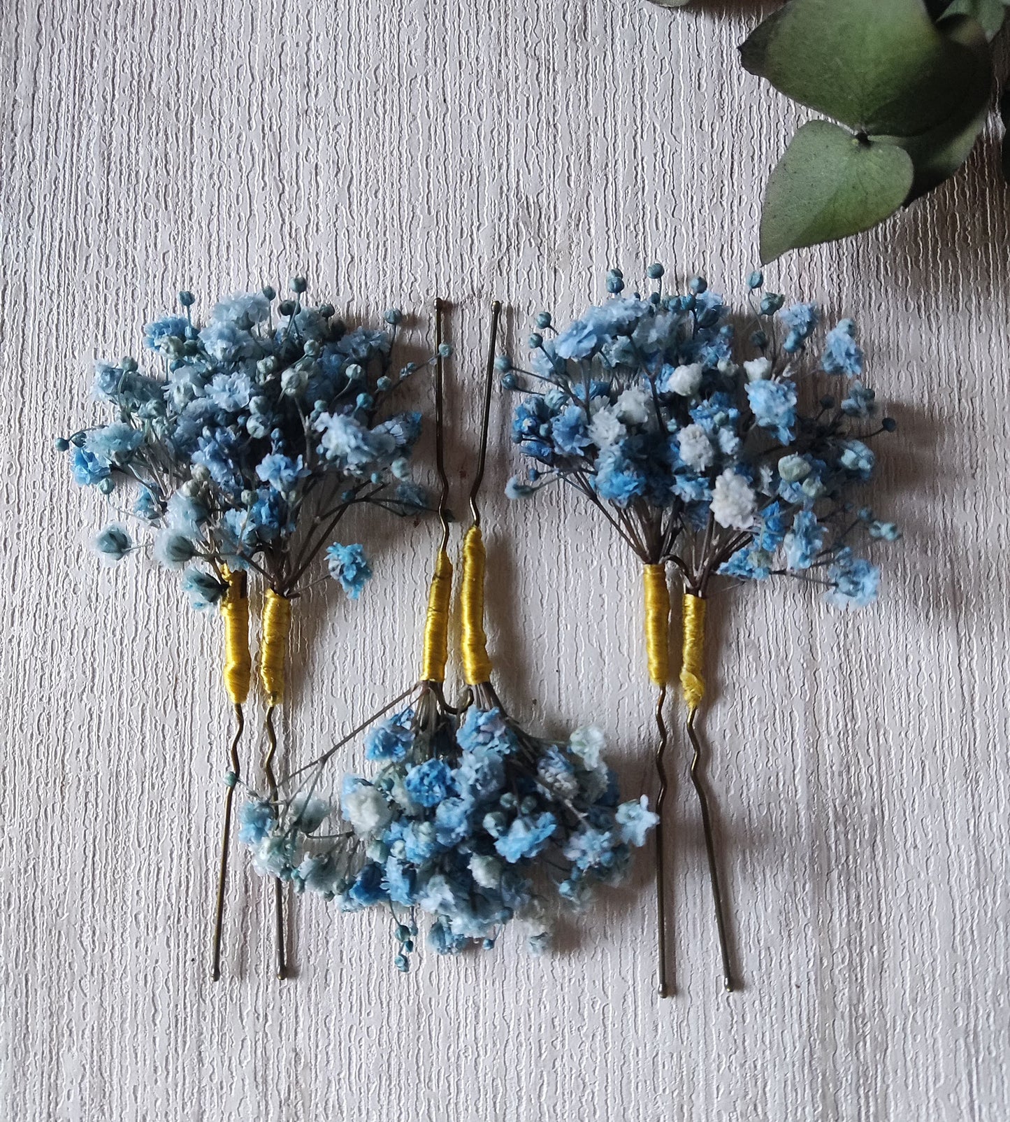 Tres horquillas con paniculata azul cielo en fondo de madera y rama de eucalipto.