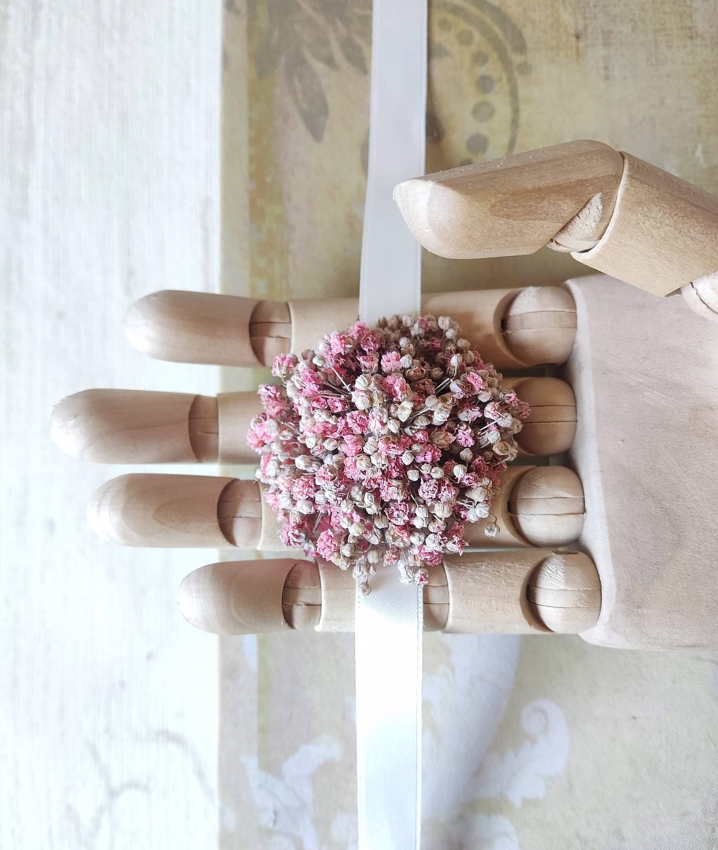 Corsage de paniculata blanca sostenido sobre los dedos de mano de madera articulada.