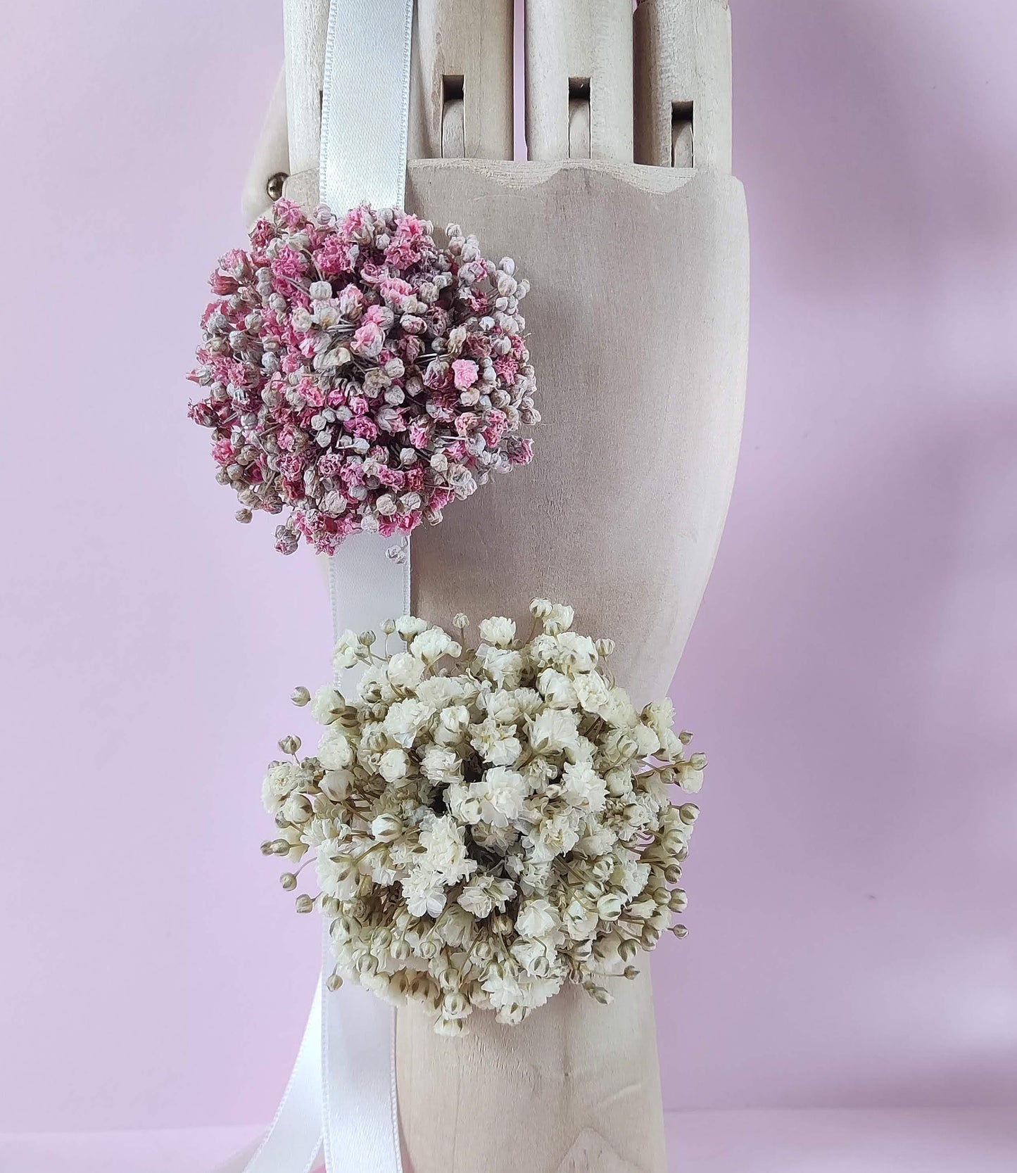 Corsages con paniculata blanca y rosa sobre mano de madera articulada.
