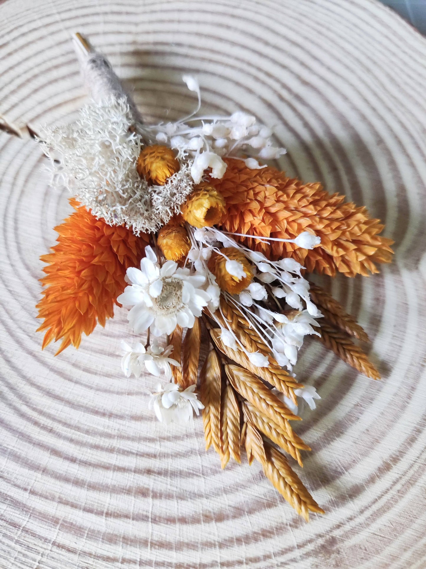 Ramillete de solapa con flores preservadas en tonos naranja y marfil sobre base de madera