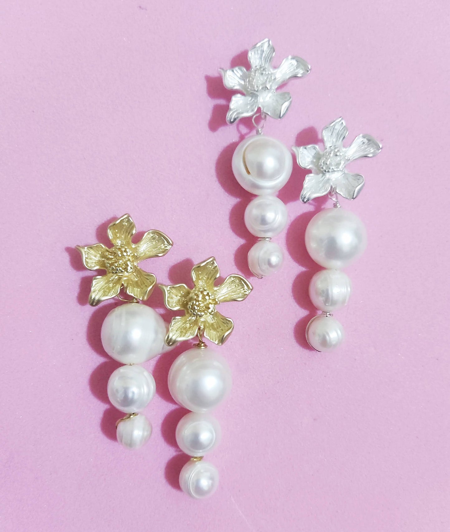 Primer plano de pendientes dorados y plateados con flor de latón y perlas de agua dulce sobre fondo rosa claro.