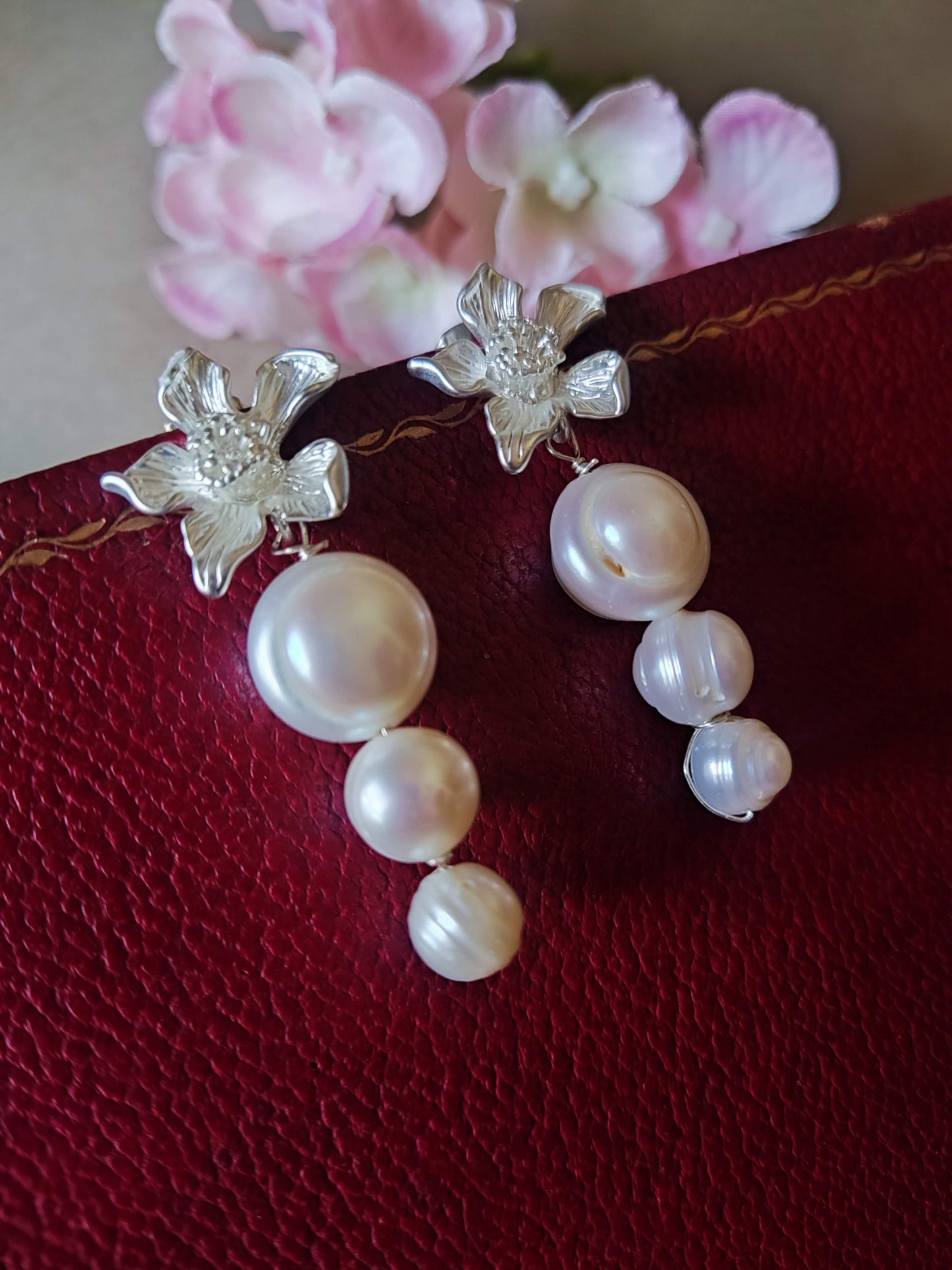 Pendientes plateados con flor de latón y perlas de agua dulce sobre fondo rojo.