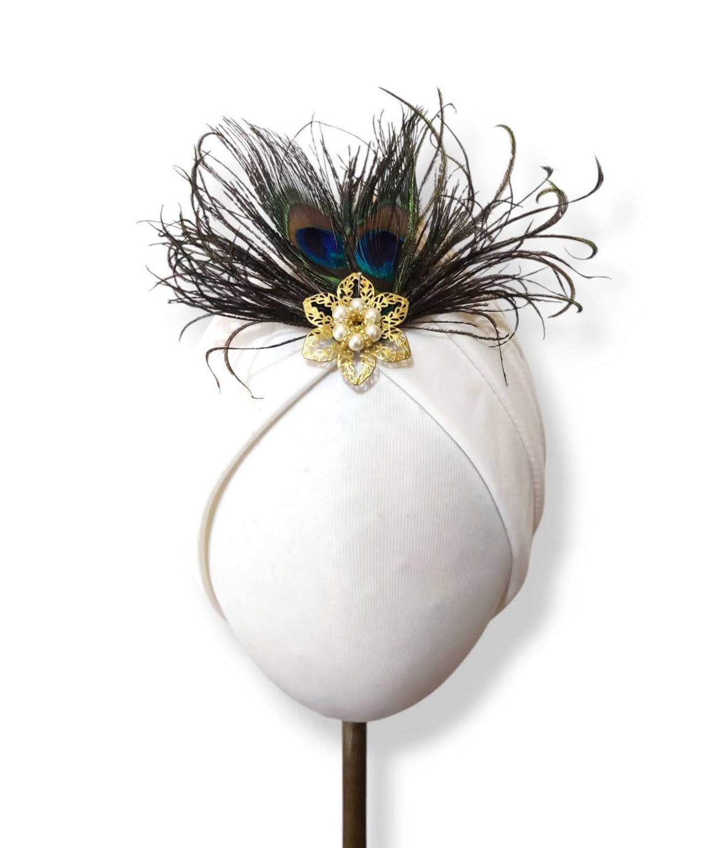Turbante color marfil con plumas de pavo real y adorno dorado.