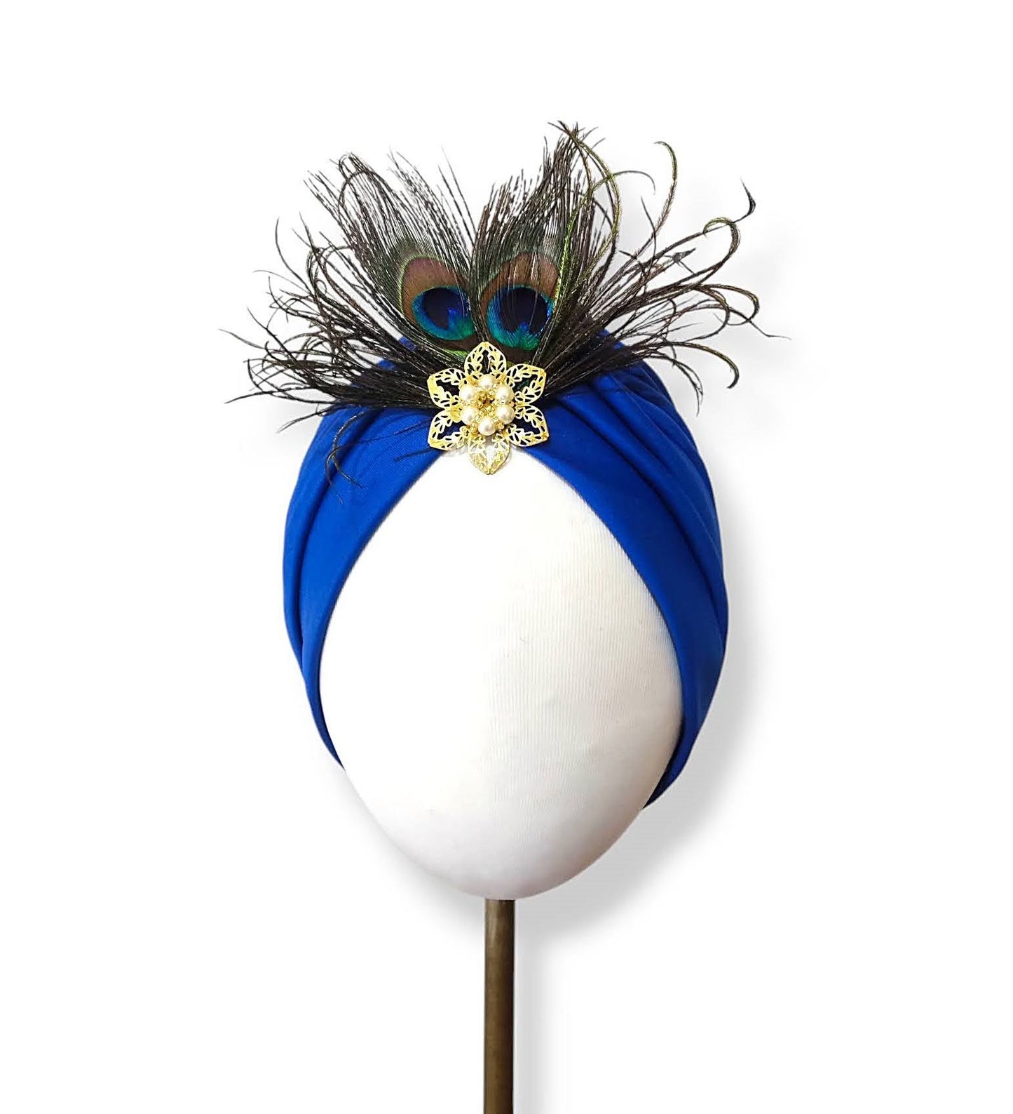 Turbante en azul royal con plumas de pavo real y broche dorado con perlas.
