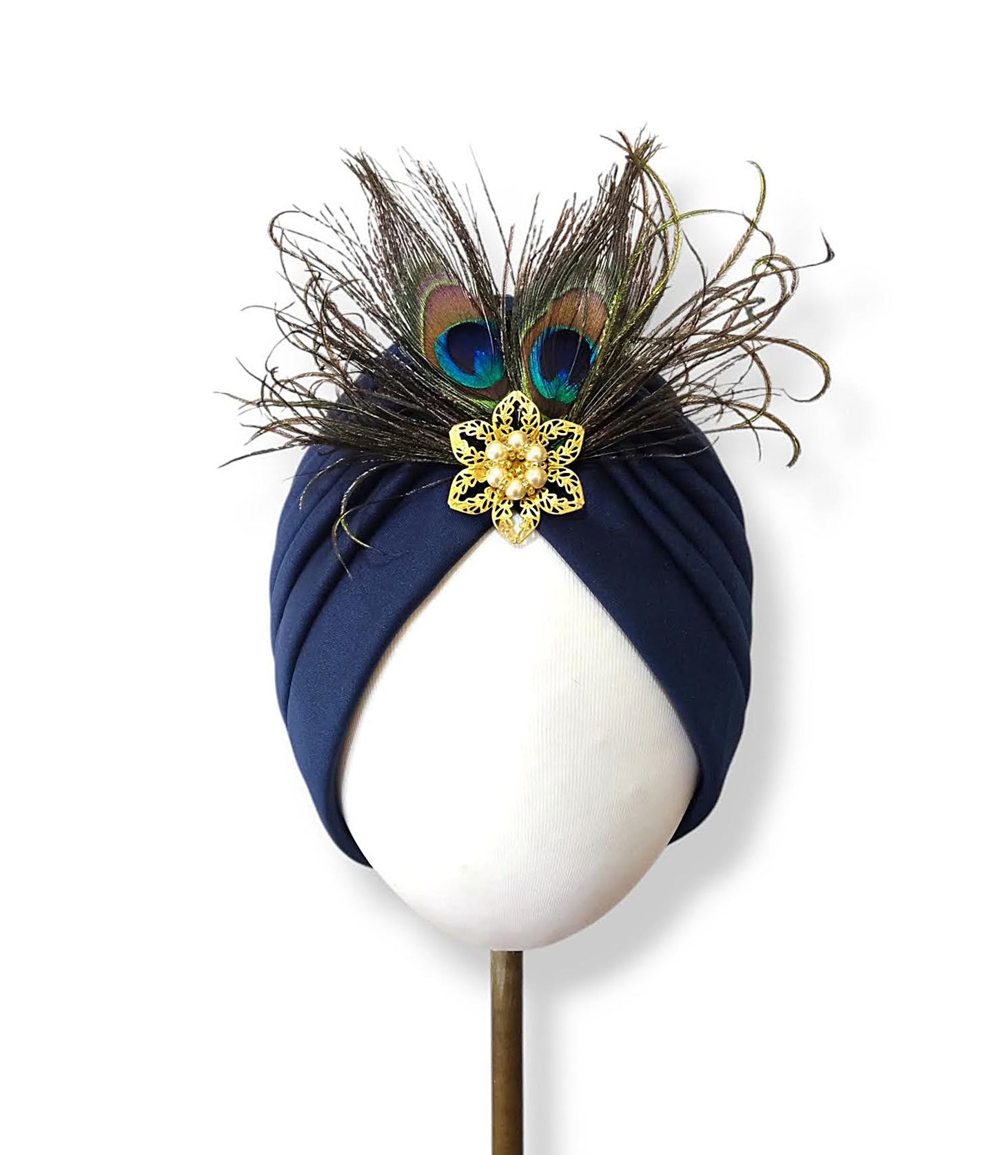 Turbante azul marino con plumas de pavo real y broche dorado.