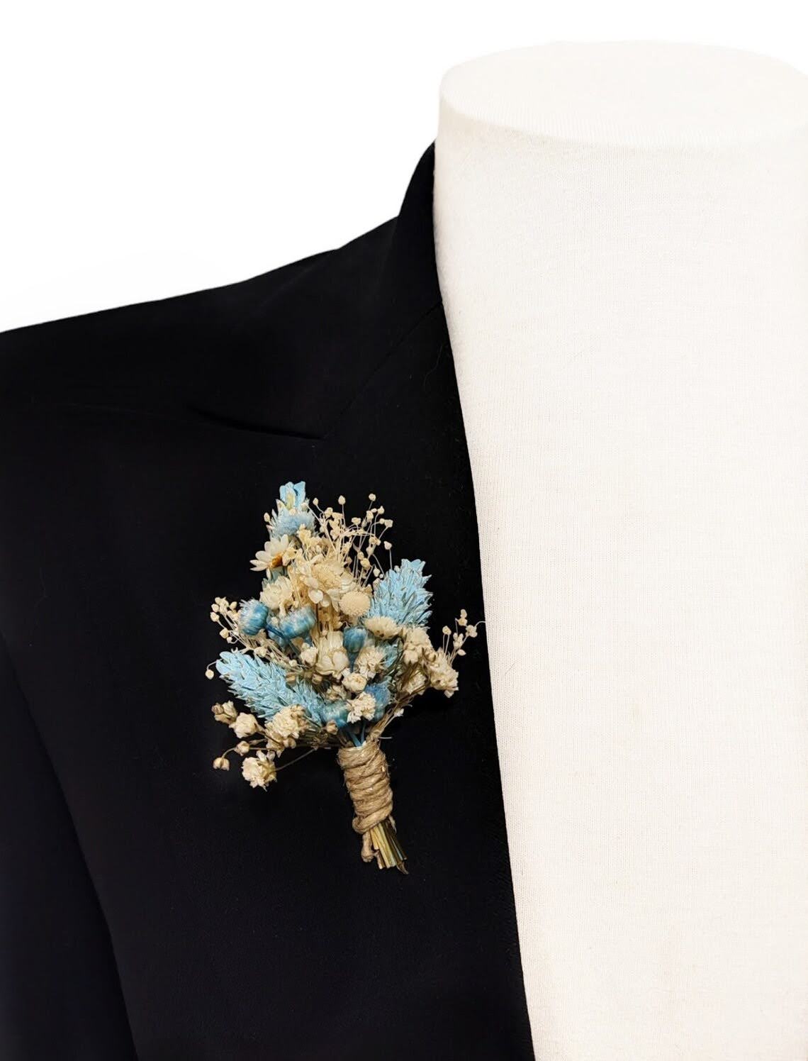 Boutonniere azul celeste y marfil colocado en la solapa de una chaqueta.