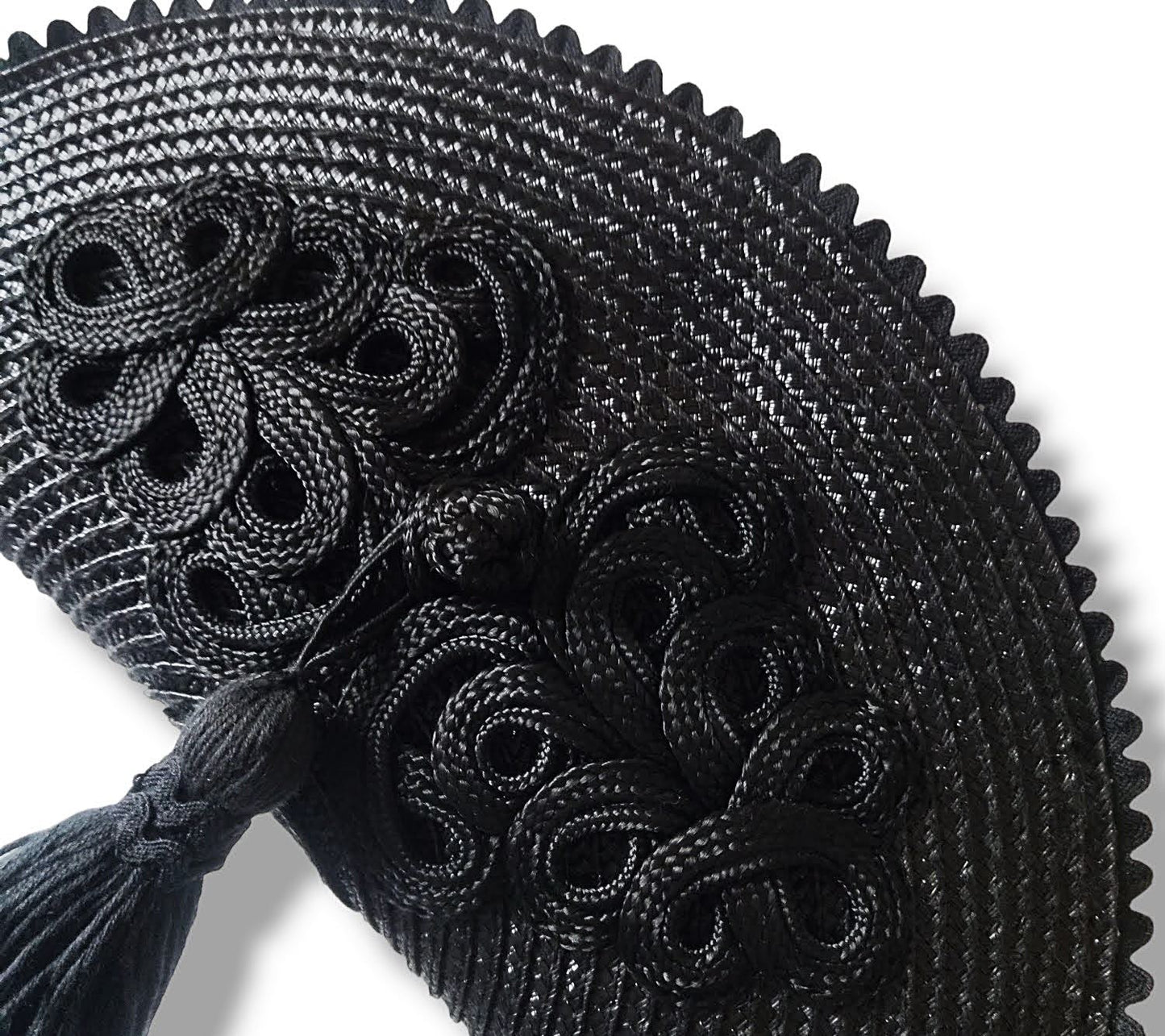 Primer plano de un bolso de paja negro con detalle de alamar trenzado, borla colgante y borde de ondulina.