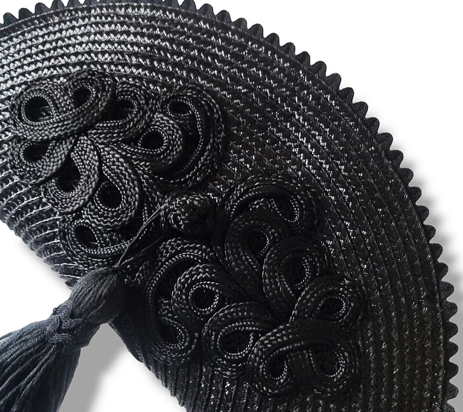 Primer plano de un bolso de paja negro con detalle de alamar trenzado, borla colgante y borde de ondulina.