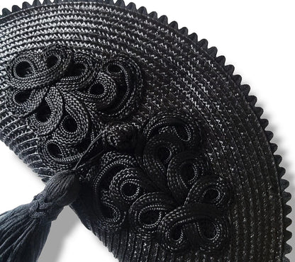 Primer plano de un bolso de paja negro con detalle de alamar trenzado, borla colgante y borde de ondulina.