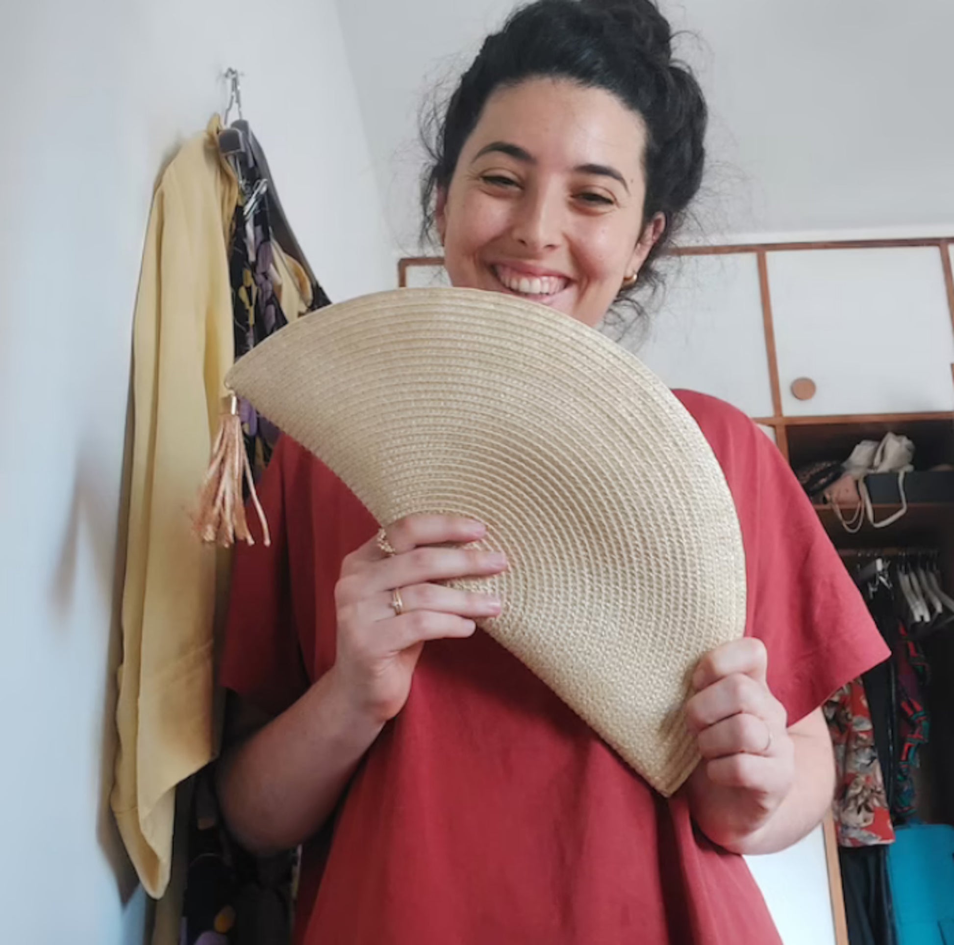Donna sorridente che tiene in mano una borsa a ventaglio in paglia naturale con nappina. Pochette artigianale Glo&Sons, perfetta per matrimoni, eventi o look estivi eleganti.