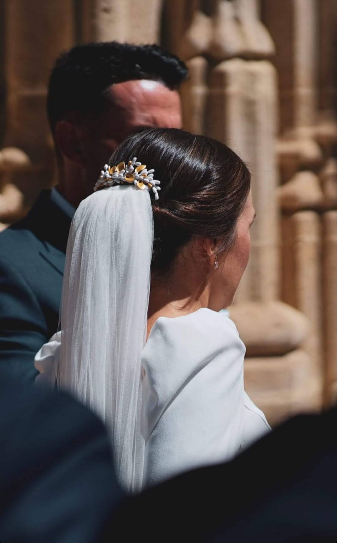 Dekorativer Brauthaarkamm mit weißen und goldenen Porzellanblüten und Knospen, auf einem niedrigen Dutt getragen, um den Schleier zu ergänzen. Handgefertigtes Design von Glo&Sons