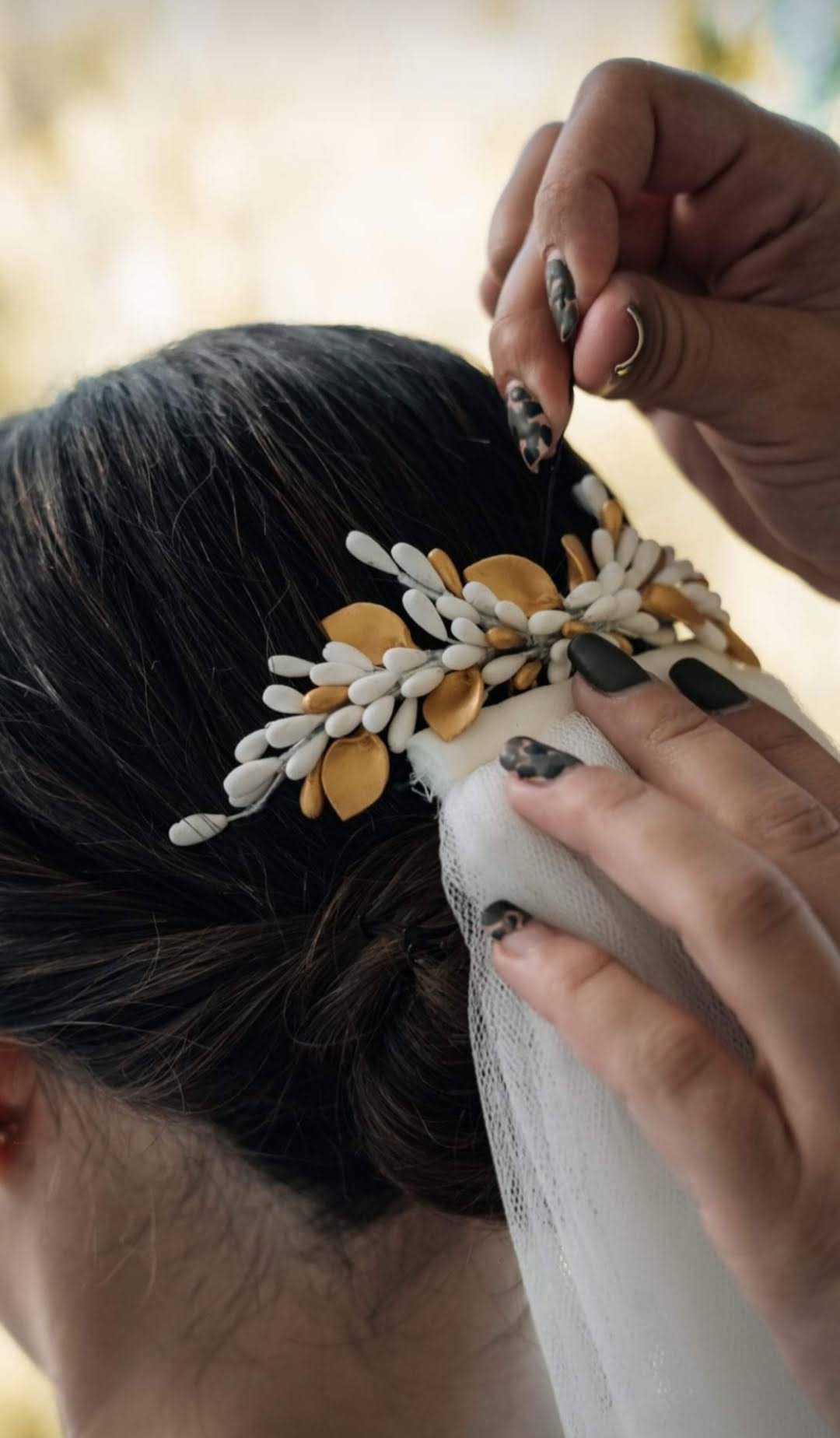 Decorative bridal hair comb with white and gold porcelain petals and buds, placed over a low updo to complement the veil. Handmade design by Glo&Sons