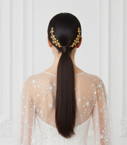Bride wearing golden porcelain star hair combs on a sleek ponytail, photographed from the back against a white ornate wall.