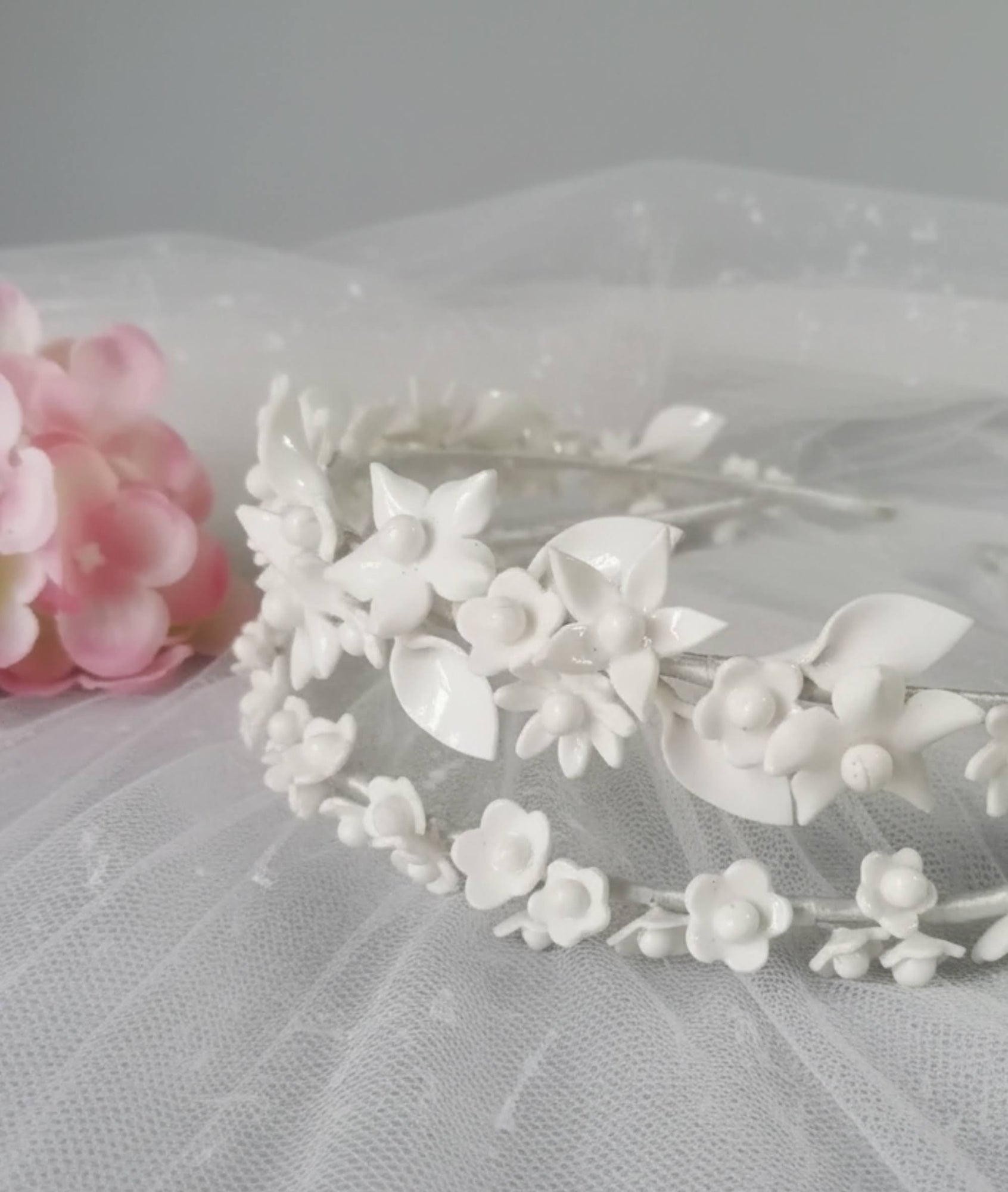 Primer plano de una diadema de novia donde se aprecian los detalles artesanales de las flores y hojas de porcelana fría blanca sobre un fondo de tul.