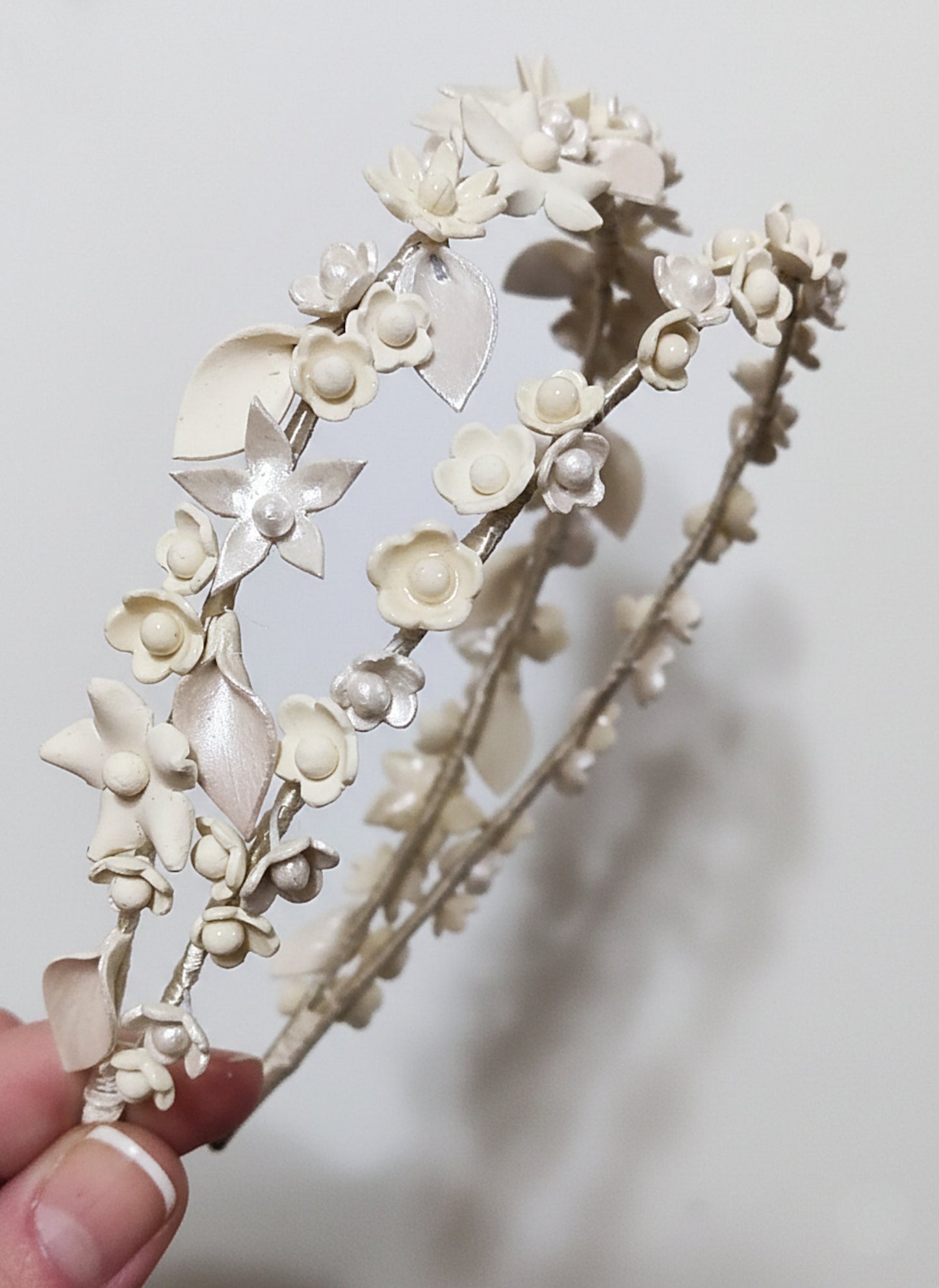 Primer plano de una diadema doble de novia en color marfil, mostrando el detalle de las flores de porcelana, las hojas nacaradas y el acabado hecho a mano.