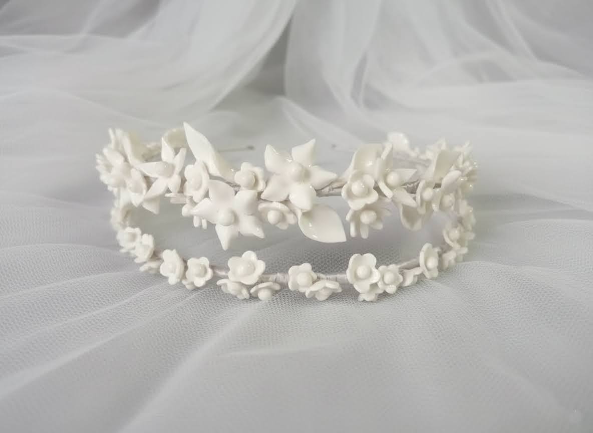 Primer plano detallado de una diadema doble de novia con flores de porcelana blanca, mostrando la textura artesanal sobre tela de tiul.