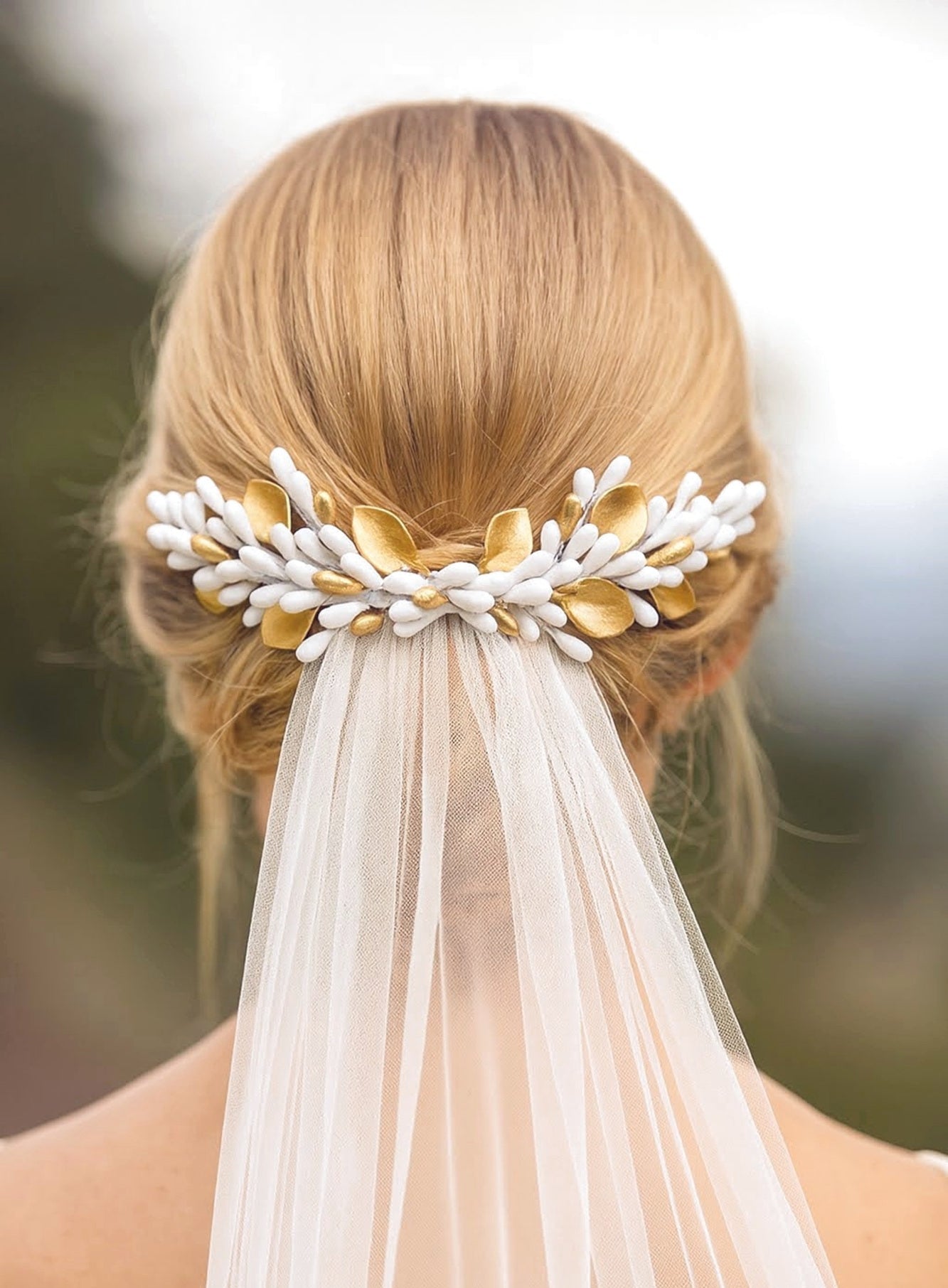 Peineta decorativa de novia con pistilos y hojas de porcelana blanca y dorada, colocada sobre un recogido bajo para completar el peinado con velo. Diseño artesanal de Glo&Sons