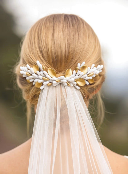Peineta decorativa de novia con pistilos y hojas de porcelana blanca y dorada, colocada sobre un recogido bajo para completar el peinado con velo. Diseño artesanal de Glo&Sons