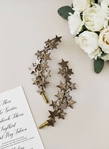 Pareja de peinetas de estrellas artesanales en color bronce junto a un ramo de flores blancas y una invitación de boda