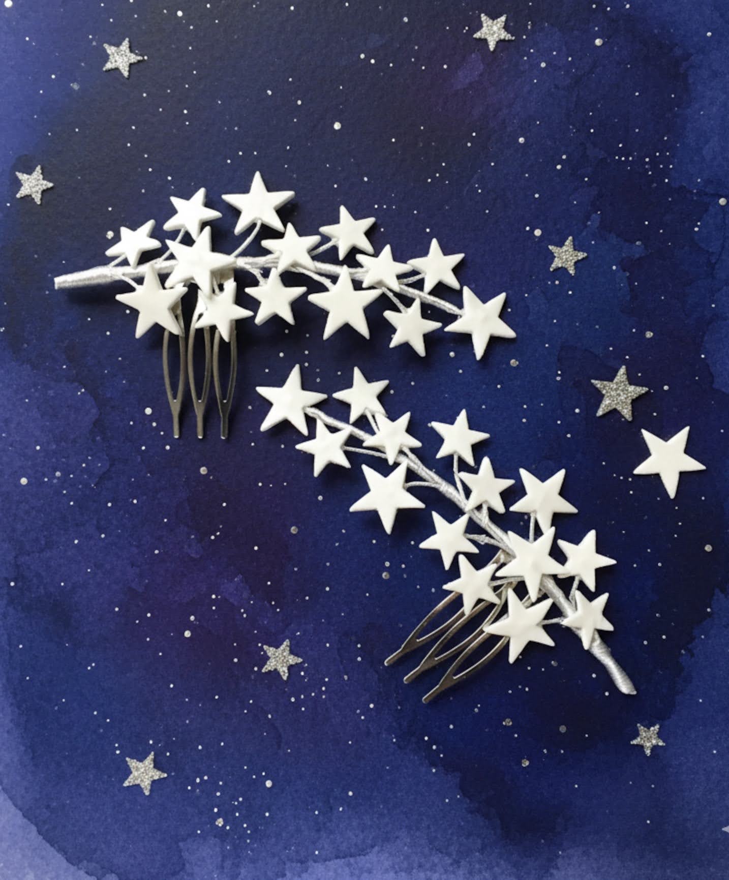 Pareja de peinetas de estrellas en porcelana fría blanca sobre un fondo artístico azul noche.