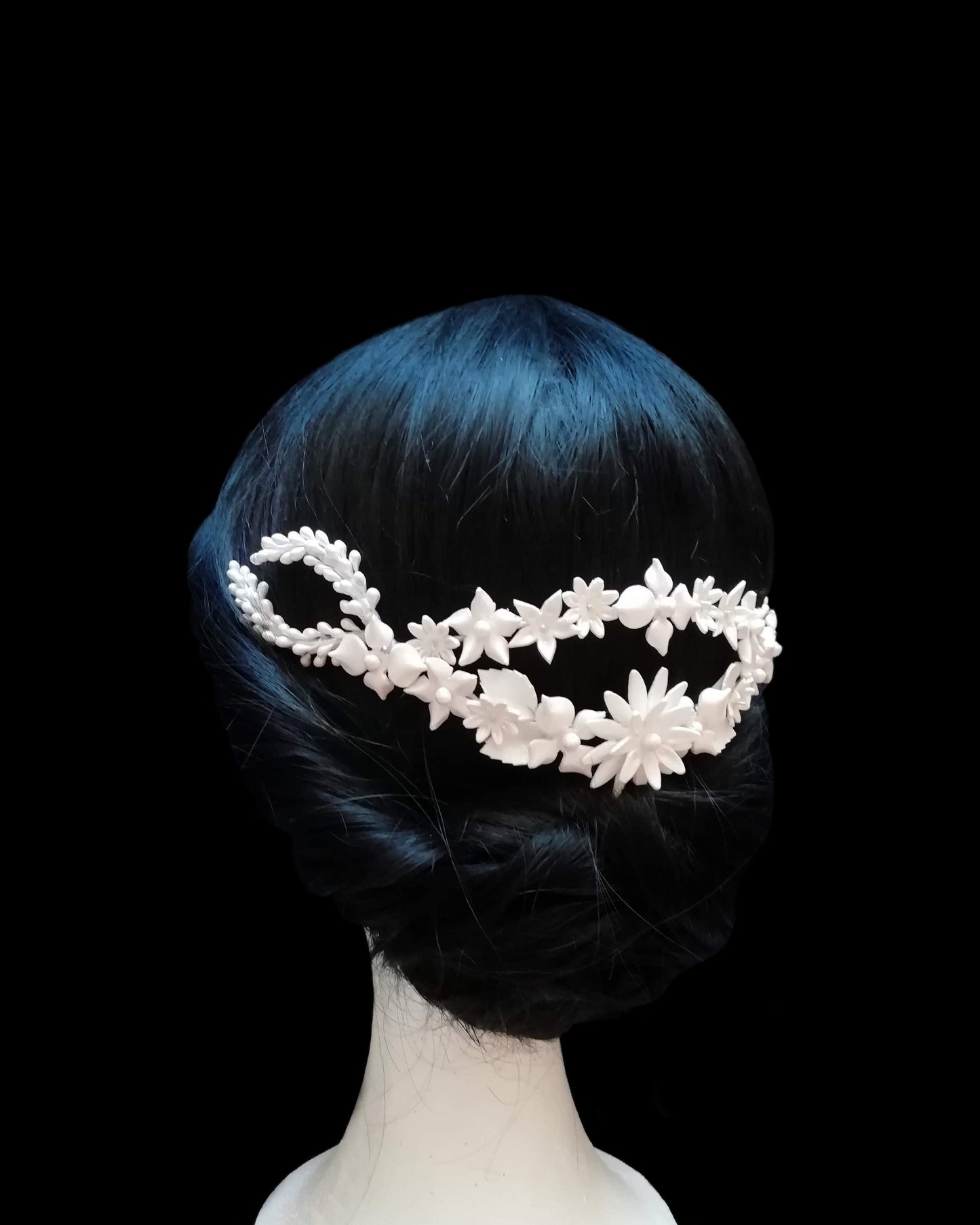 Tiare arrière de mariée en porcelaine blanche, ornée de fleurs et de feuilles délicates, portée sur un chignon bas élégant. Design fait main par Glo&Sons.