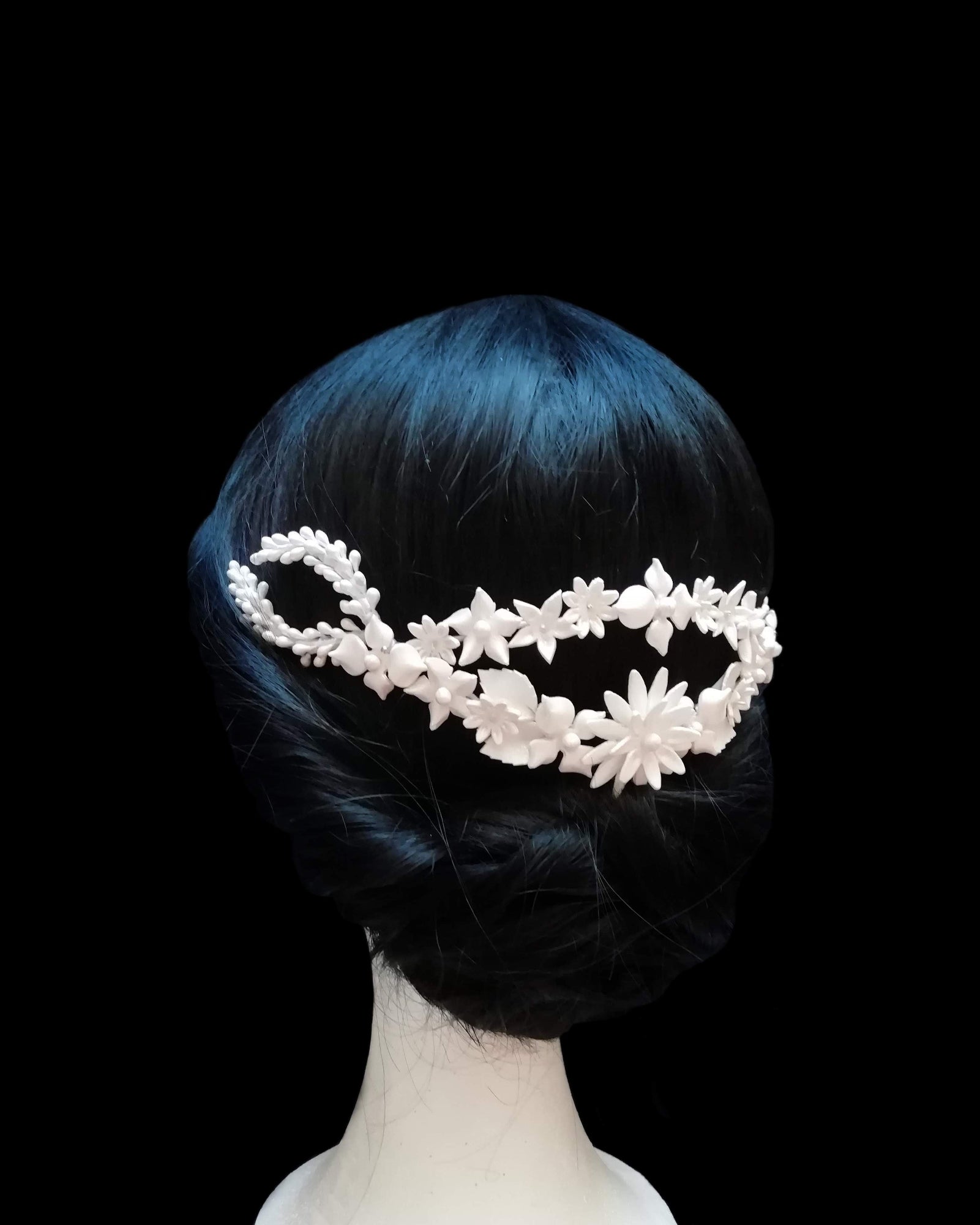 Tiare arrière de mariée en porcelaine blanche, ornée de fleurs et de feuilles délicates, portée sur un chignon bas élégant. Design fait main par Glo&Sons.